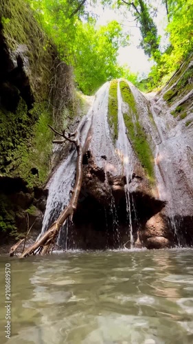 The water flows down the mossy rocks, forming several waterfall streams that fall into a clear reservoir in the middle of a dense forest. Concept: Forest waterfall, wildlife, cleanliness and freshness