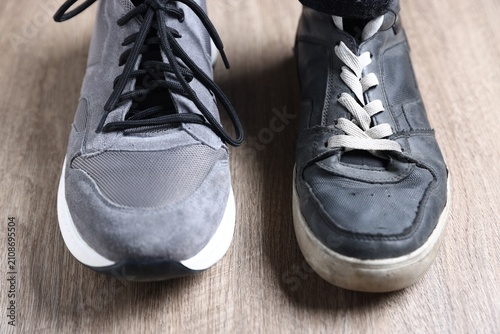 Εκτύπωση καμβά New grey sneaker and old athletic footwear on wooden floor, closeup