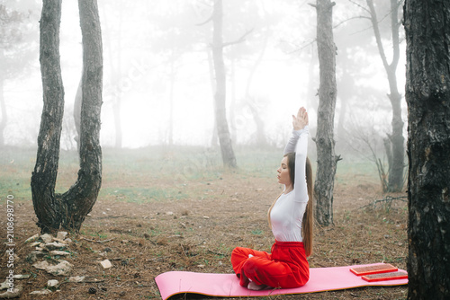 Side view of a woman meditating with raised hands in a misty forest