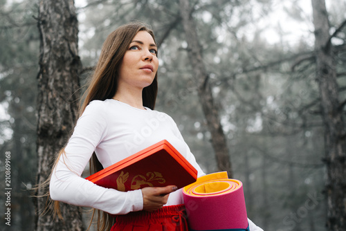 Portrait of a woman holding a yoga mat and sadhu boards in a forest