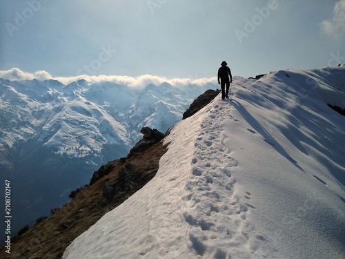 Obraz na płótnie Lone hiker walking along a snowy mountain ridge with panoramic views of the Italian Alps during a winter hike,  Lombardy, Italy