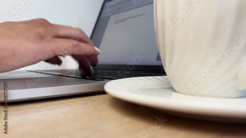 Female hands with neat manicure typing on laptop keyboard on wooden table next to white cup of coffee. Concept: Remote Work, Cozy Workplace, Coffee Break, Productivity. High quality 4k footage
