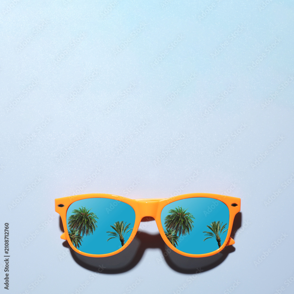 Obraz premium Sunglasses with reflection of tropical palm trees and blue sky on light blue background. Space for text
