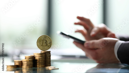 A person is holding a cell phone and looking at a coin on top of a pile of coins