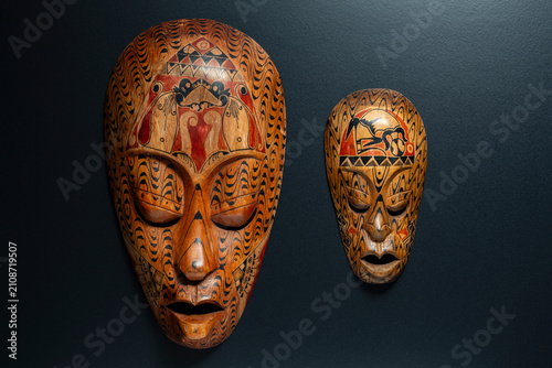 Pair of handcarved ethnic african wooden masks with intricate tribal patterns and geometric ornaments hanging on dark wall, closeup, ideal for interior decor, travel, and cultural concepts