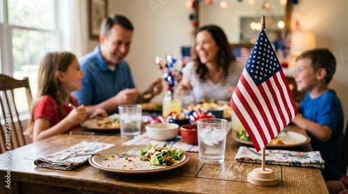 Close-up of American flag on dining table with blurred happy diverse family celebrating in background.