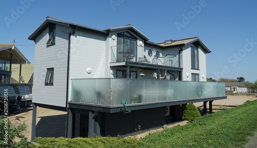 Contemporary, reversed-accommodation home in Felixstowe on stilts features grey composite cladding and a large, glass-paneled balcony