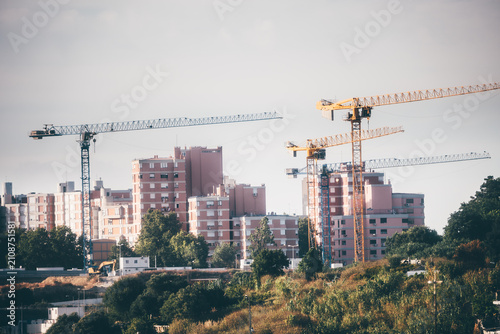 Photography Telephoto cityscape of several tower cranes surrounding pink residential apartme