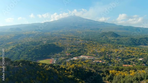 Nicolosi, Sicily, Italy. Mount Etna, volcanic craters overgrown with dense forest, aerial panoramic view under a bright blue sky with scattered clouds. Drone footage