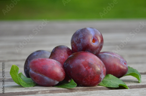 Foto Group of ripe red- purple plums (genus Prunus ) with fresh green leaves arrange on wooden surface