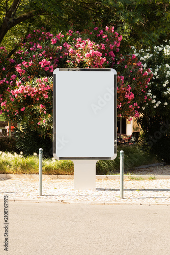 Quadro su tela Blank freestanding outdoor billboard mockup surrounded by colorful flowering shrubs in a landscaped urban setting