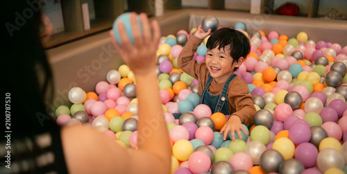 Happy asian boy playing in a ball pit with his mother, bonding and having fun