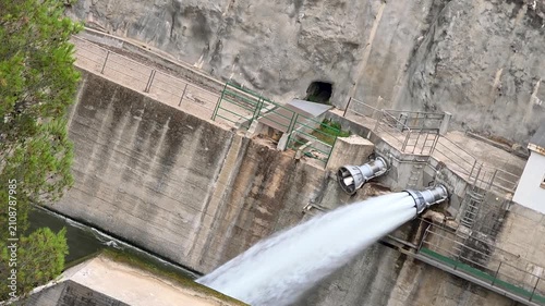 Slow motion view of massive water discharge from Beniarres dam spillway pipe into the Serpis river, powerful water flow and concrete dam wall, Spain