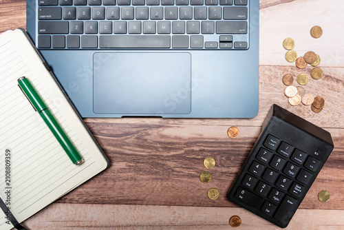Top view of a laptop keyboard, coins, a pen, and a notebook with blank pages.