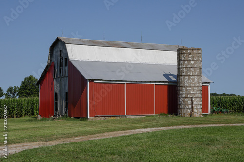 Red barn on a rural farm among the mid-west corn fields. Barns are red in color as farmers would add rust to paint to kill fungi.