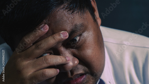 Fotografía An intense macro portrait shows an exhausted adult Asian male covering the face with one hand in deep sorrow