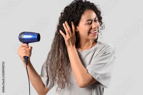 Beautiful young happy African-American woman blow drying her healthy curly ha...