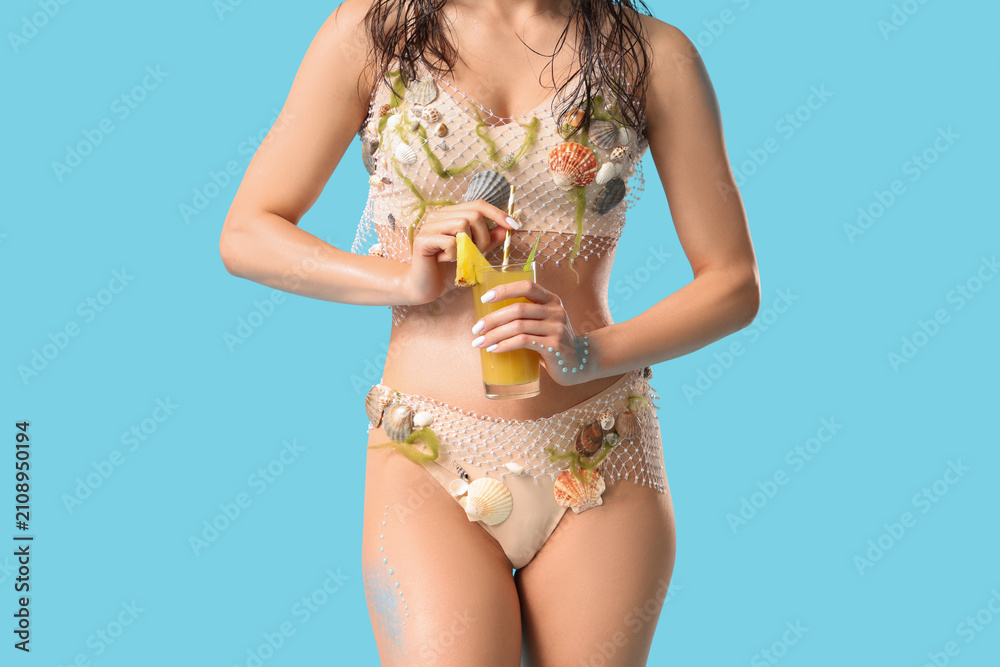 Obraz premium Beautiful young woman dressed as mythical mermaid with glass of pineapple juice on blue background, closeup