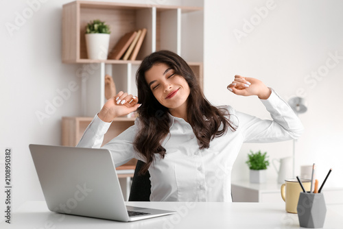 Beautiful young happy businesswoman with laptop stretching her hands at office