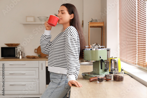 Beautiful young woman with modern coffee machine and cup of cappuccino in kit...