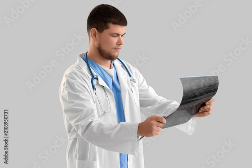 Male doctor studying x-ray image of spine on light background