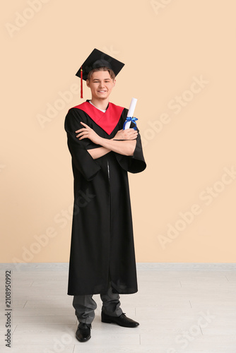 Happy male graduate with diploma on beige background