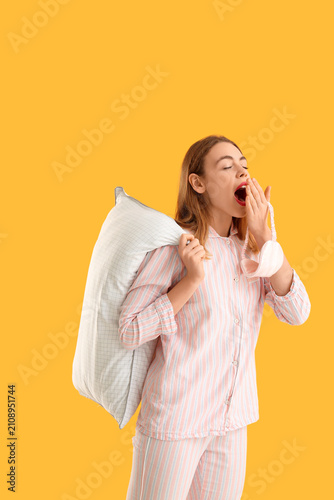 Beautiful young woman with white soft pillow and sleep mask on orange background