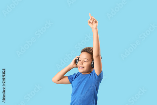 Little African-American boy with headphones listening to music on blue background