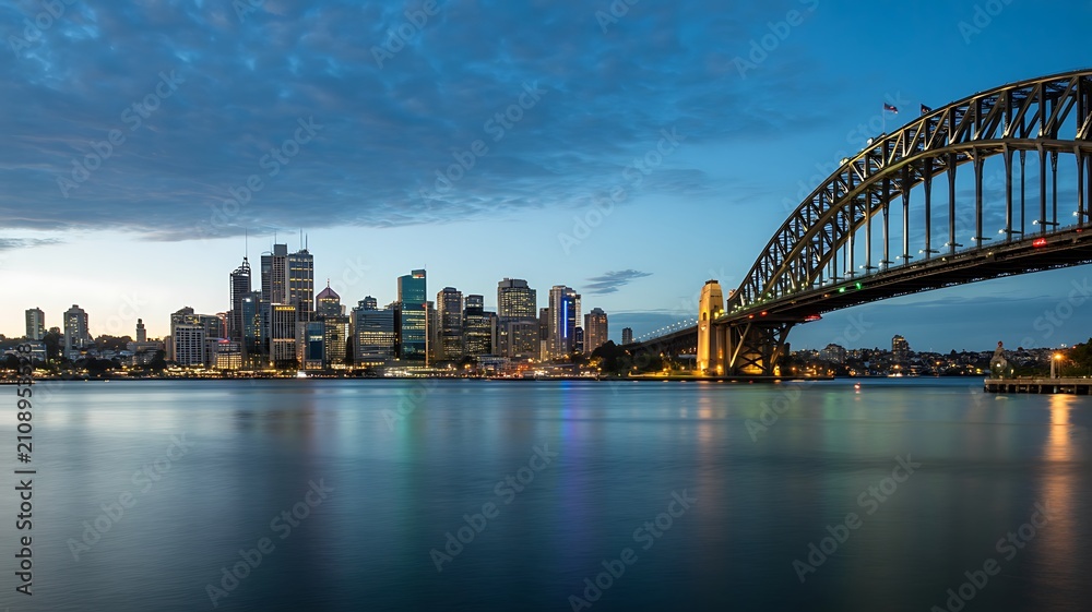 Naklejka premium Sydney harbour bridge with city skyline reflected on calm waterfront at dusk