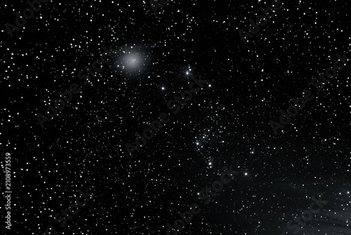 Black and white astrophotography featuring a dense star field and a distant galaxy cluster