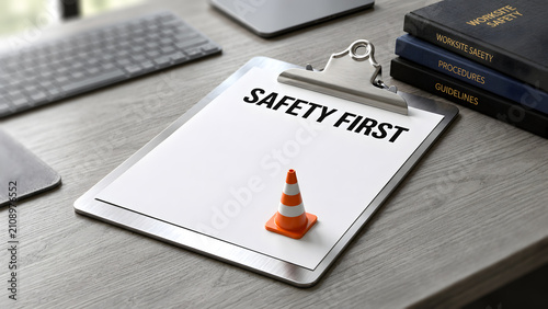 Safety first concept with clipboard and miniature traffic cone on office desk representing workplace hazard prevention and compliance guidelines.