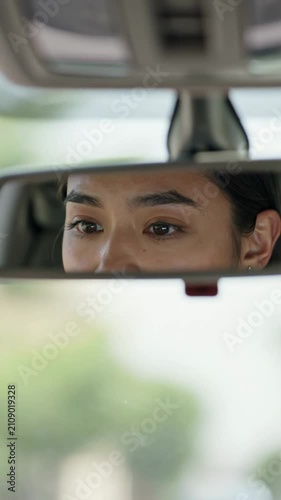 Close-up of a woman’s eyes visible in the rearview mirror of a car, with her eyebrows raised and a focused expression, vertical shot