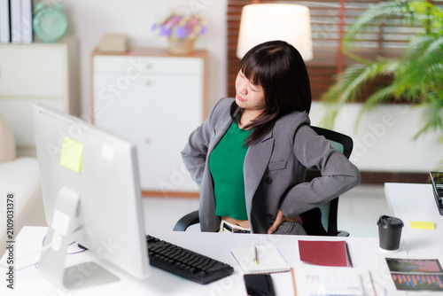 Fotografie Young asian woman experiencing sudden back pain or ache while working at a home office