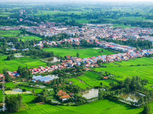 Fotografía A high-angle aerial landscape shows a rural settlement nestled among lush green farmland and ponds