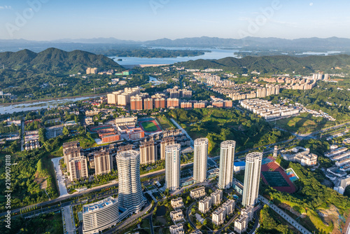 Принти на полотні An aerial shot of a developed urban area with high-rise buildings, nestled among green mountains and a large lake under a clear sky