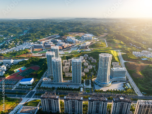 Photos A high-angle aerial shot showing modern urban buildings adjacent to natural green hilly landscapes and infrastructure