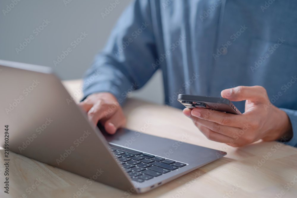 Fototapeta premium Close Up of Person Using Smartphone While Working on Laptop, Remote Work, Business Technology, Digital Communication, and Productivity Concept