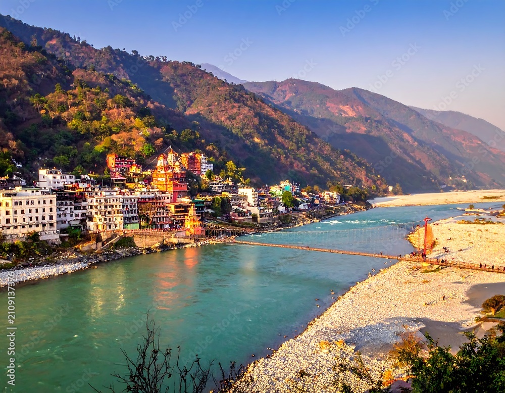 Fototapeta premium A vibrant scenic view of a river cutting through a valley with mountains. Colorful buildings line the riverbank