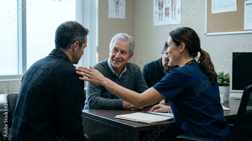 Caring nurse discussing health with male patients and family in a medical office