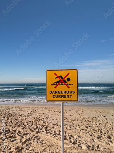 No swimming dangerous current sign at beach on perfect sunny day with blue sky and waves in vertical format..