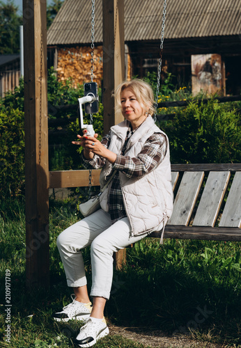 Mature woman creating smartphone video while sitting on a wooden swing outdoors