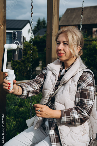 Mature woman creating smartphone video while sitting on a wooden swing outdoors