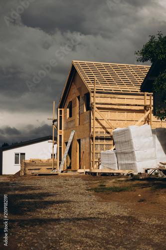 Modern wooden frame house under construction with dramatic cloudy sky