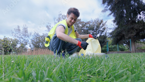 Photo of a boy wearing a reflective vest and gloves picking up trash in a park