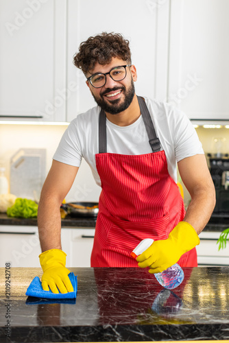 Quadro su tela Arabian man wipes kitchen counter with cleaner and microfiber cloth removing grease for hygiene and food safety