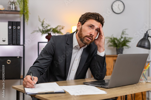Middle-aged businessman at home office checks contracts spots error facepalms and marks fix with pen. Freelancer guy at table reviews legal text writes fix signs page and breathes relief after stress.