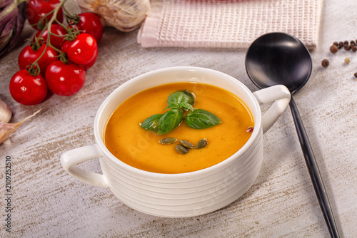 Pumpkin cream soup in white bowl with basil and pumpkin seeds