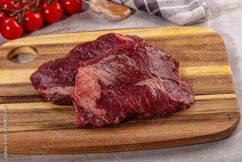 Raw beef cheek steaks on wooden cutting board with cherry tomatoes