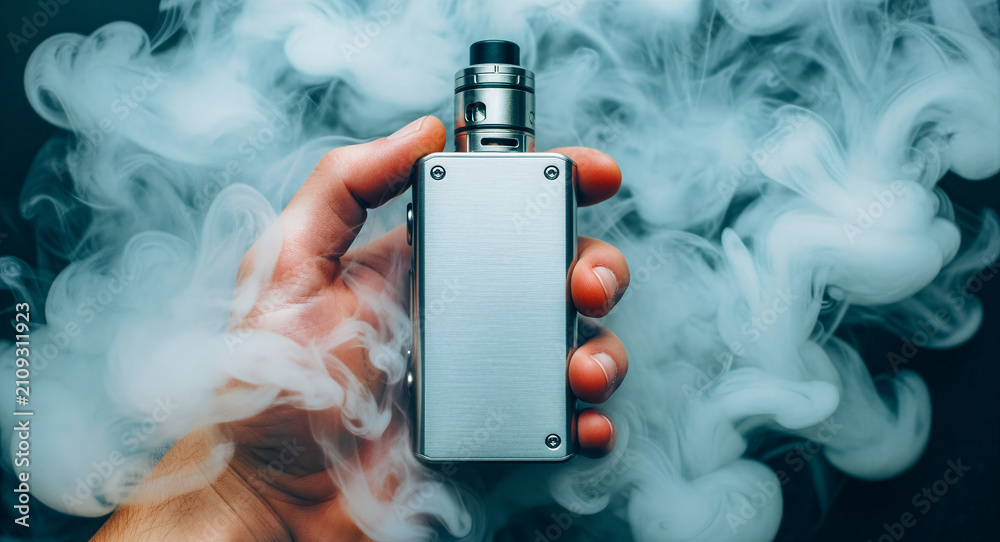 Fototapeta premium Hand holding metallic electronic cigarette in thick smoke. User with silver box mod device in dark studio. Vaping lifestyle concept for commercial marketing and health awareness.