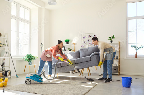 Принти на полотні Couple cleaning home vacuuming under sofa together